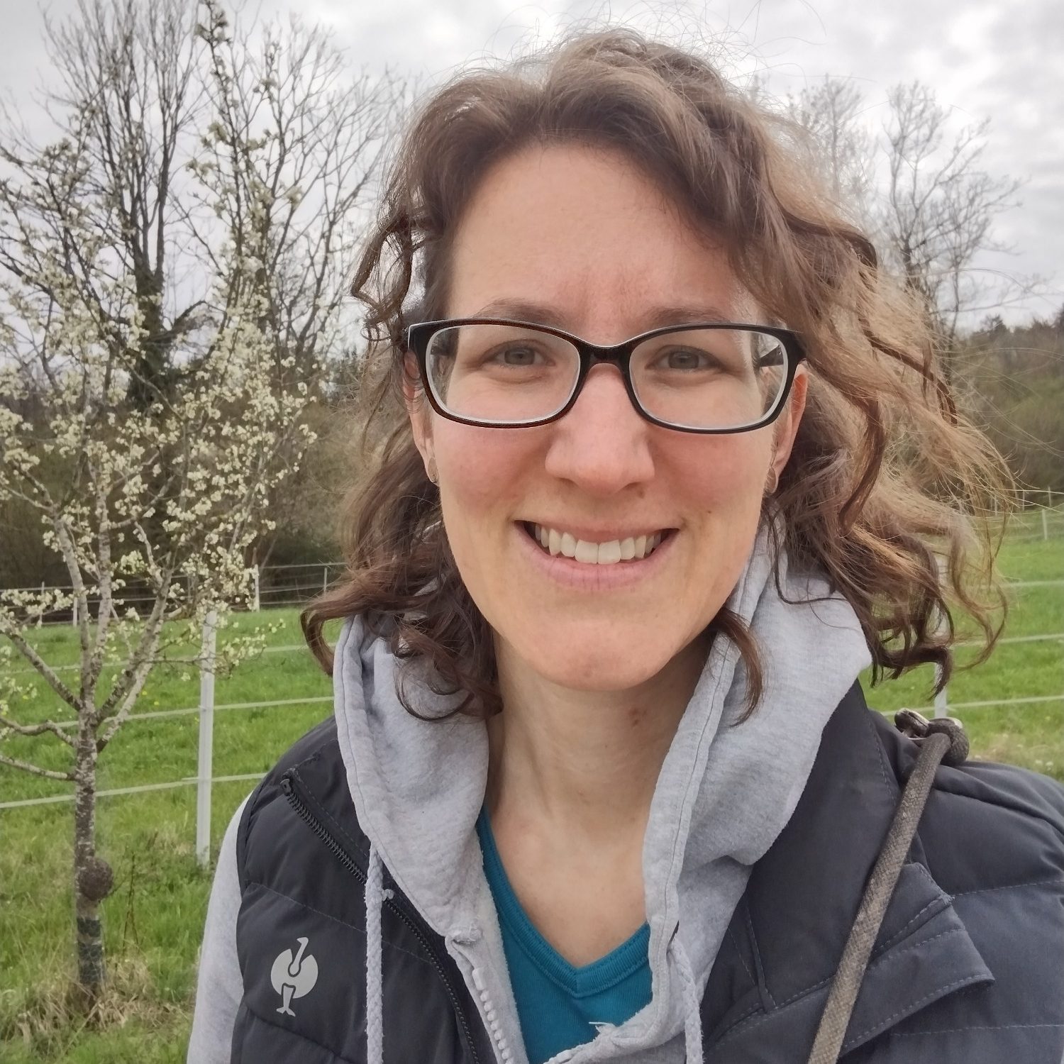 Yvis Futterberatung - ANIfit Berater aus dem Zollernalbkries Frau mit Brille und lockigem Haar vor einem Baum auf einer grünen Wiese.