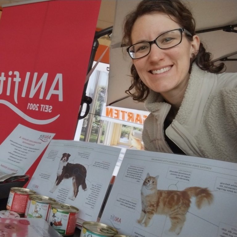 Frau mit Brille lächelt neben Präsentation von Tiernahrungsprodukten.