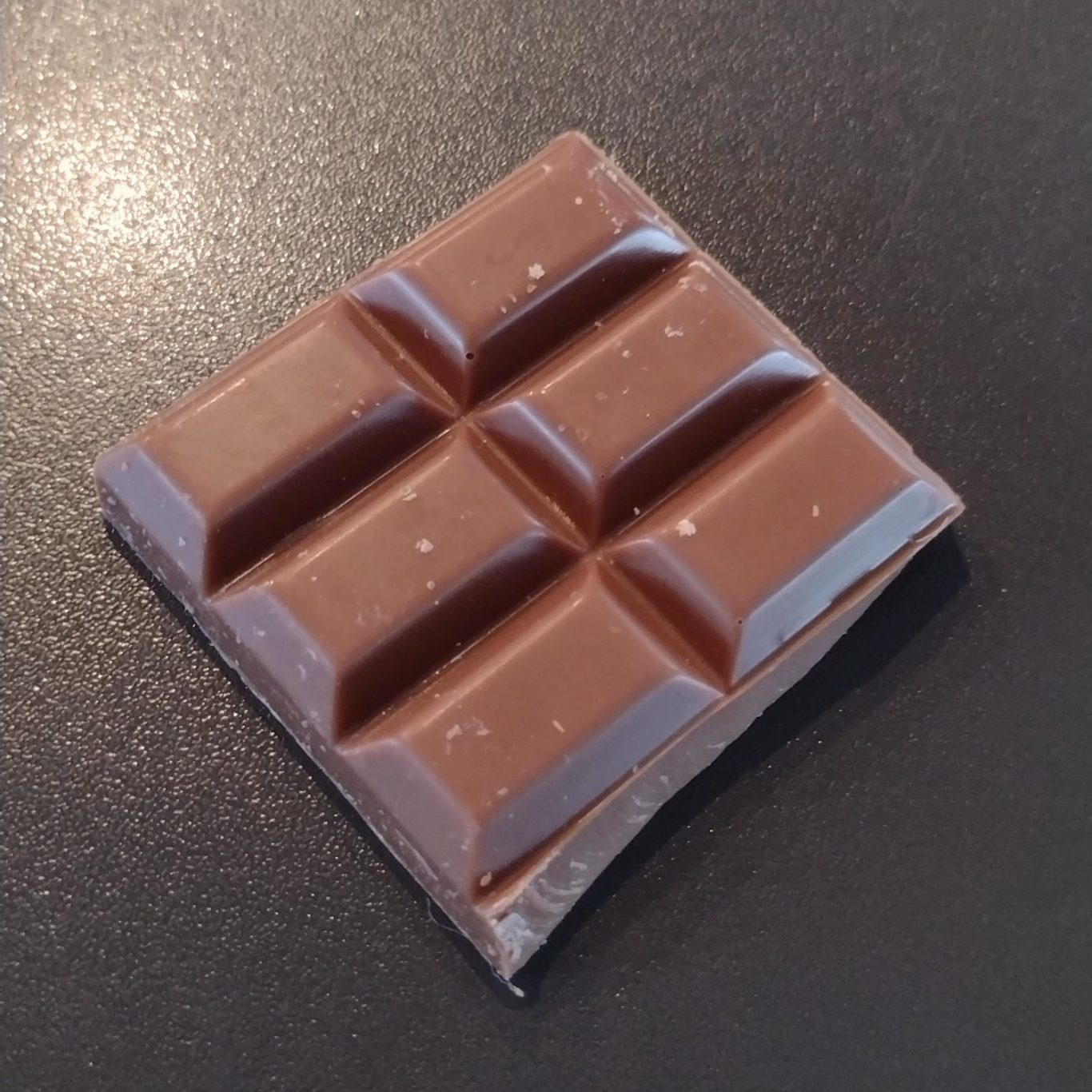 Ein Stück Schokolade mit rechteckigen Riegeln auf blauem Hintergrund.