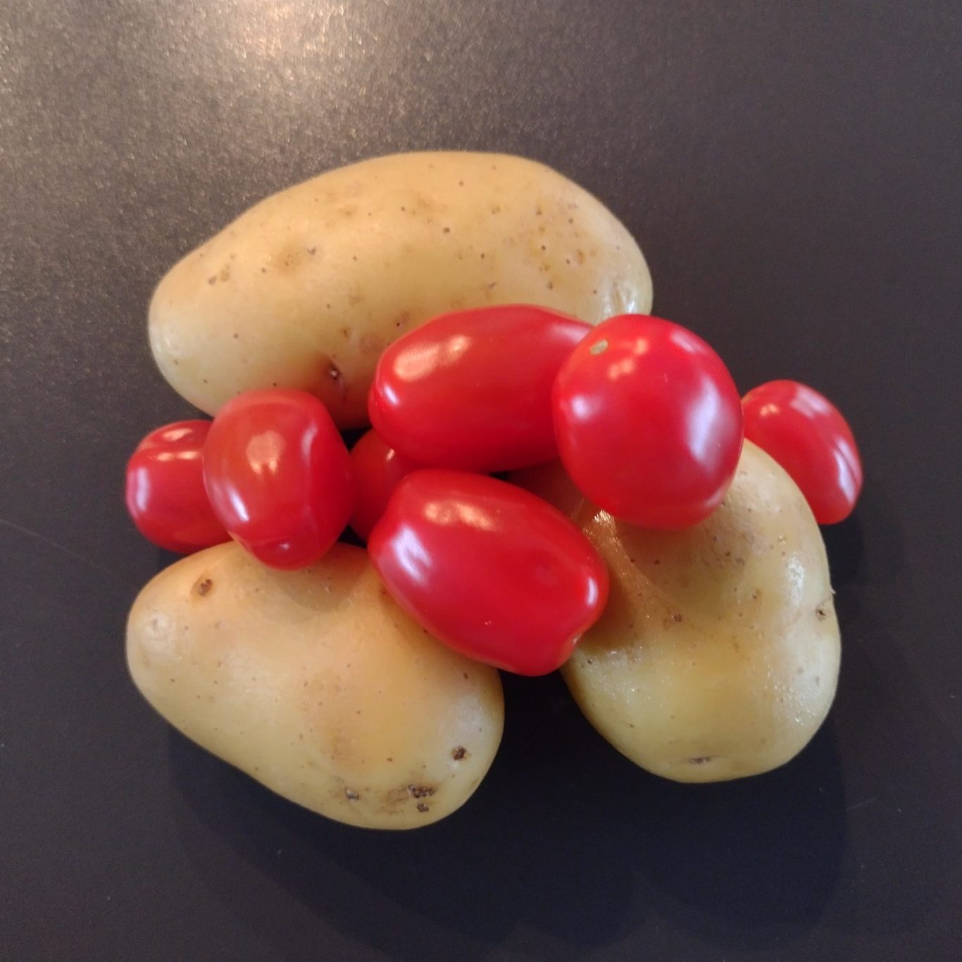 Ein Haufen Kartoffeln mit roten Kirschtomaten darauf.