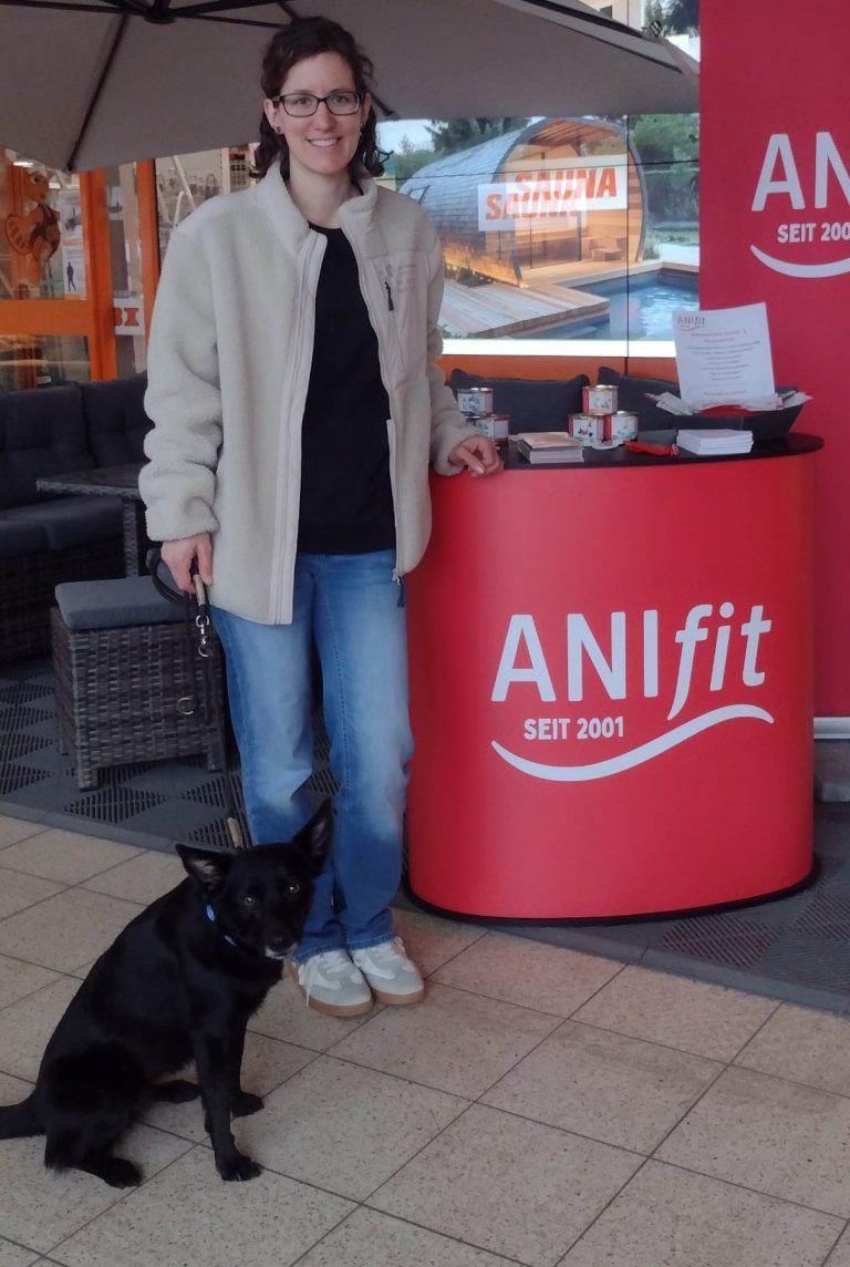 Frau mit Brille steht neben einem schwarzen Hund vor einem ANIfit-Tresen.